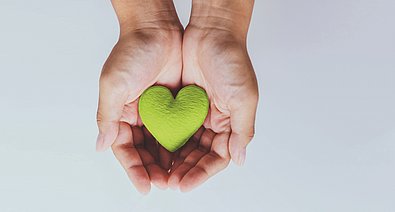 Ein grünes Herz wird in den Händen gehalten