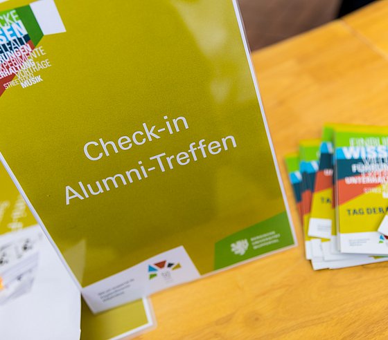 Schild mit Aufschrift Check in Alumni-Treffen